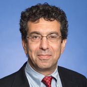 A photograph of a professor in a portrait studio with a nice tie. He wears glasses and has curly black hair.