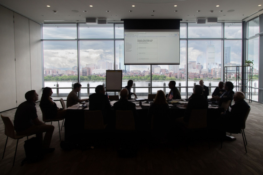 People around a table in a darkened room, watching a viewscreen