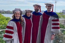 Four graduates of MIT SSP&#039;s PhD program stand on a balcony in full graduation regalia